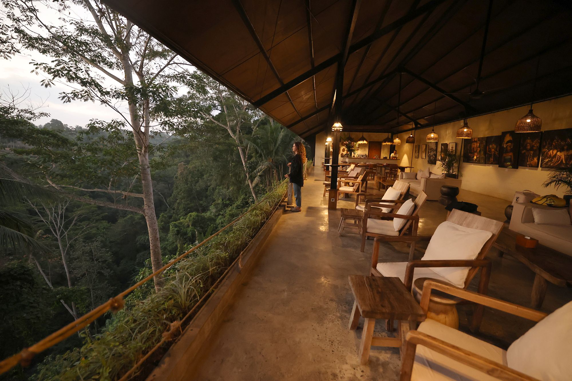 The lounge at dusk: sofas along the rail, the lamps on, the jungle dropping away beside the terrace