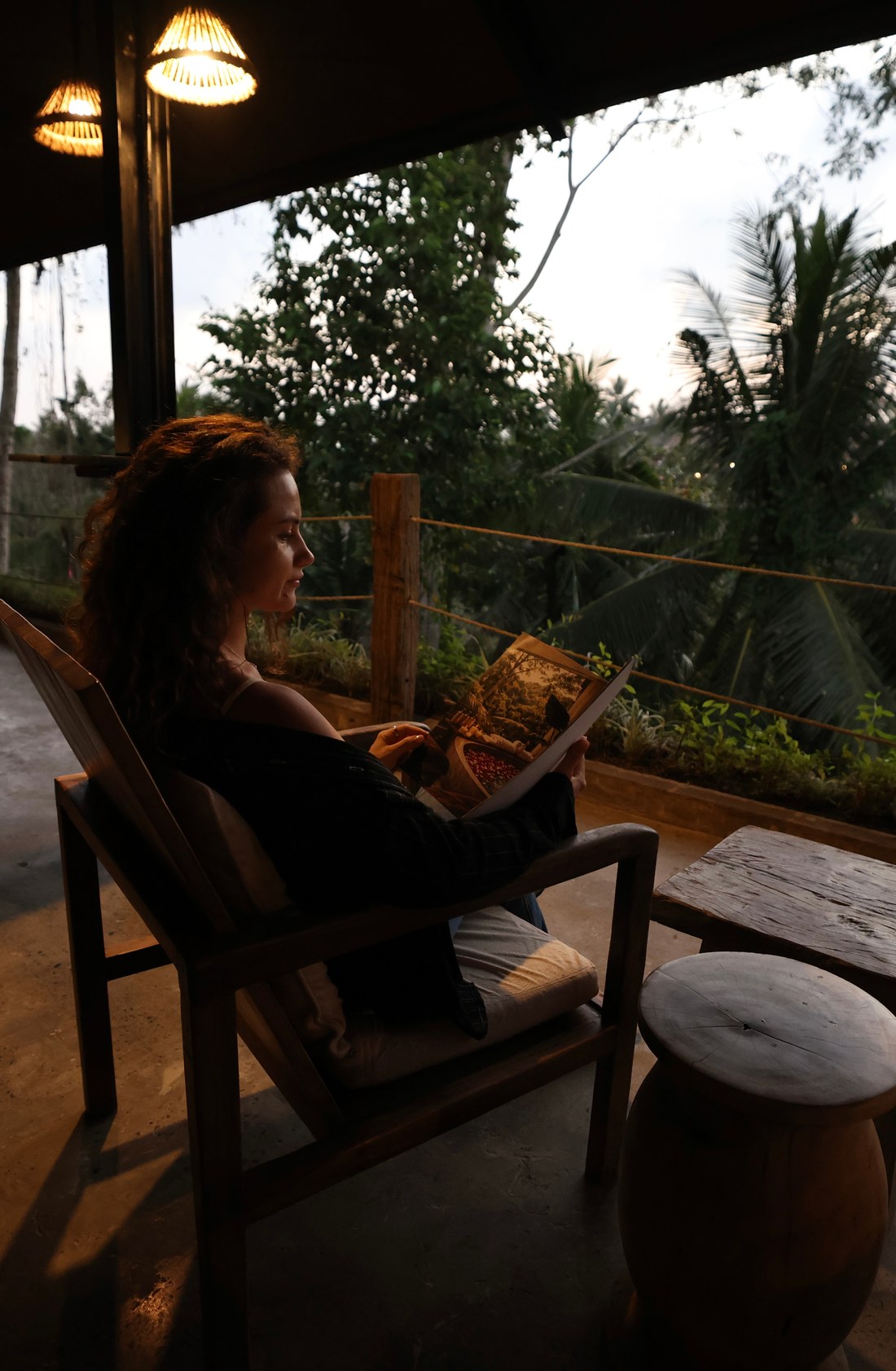 A guest reading by the rail of the lounge at dusk, the jungle behind