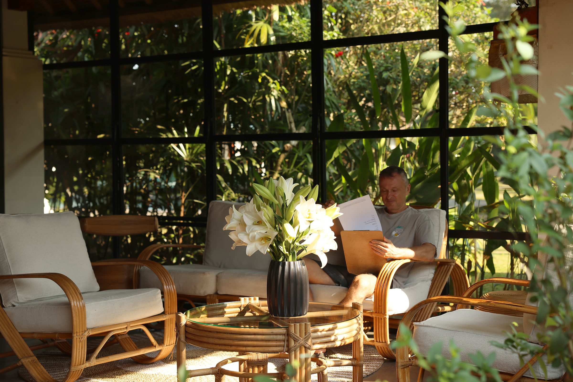 The lounge by the reception in the morning: rattan chairs, white lilies on the table, a guest reading