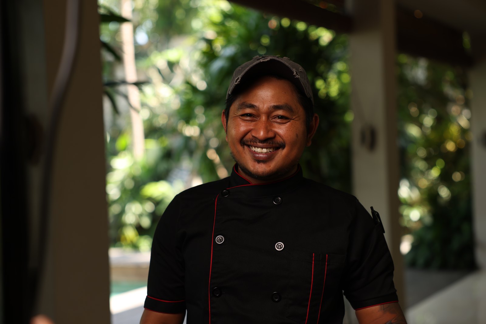 The chef in his black jacket, smiling, the pool and the jungle behind him
