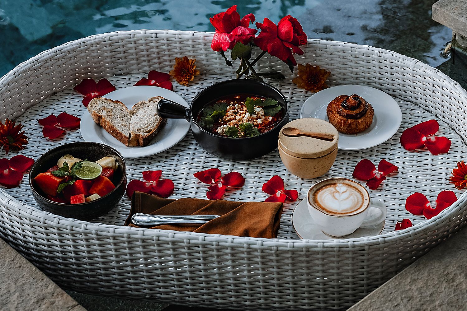 The tray from above: fruit, pastries, a bowl and a latte among petals