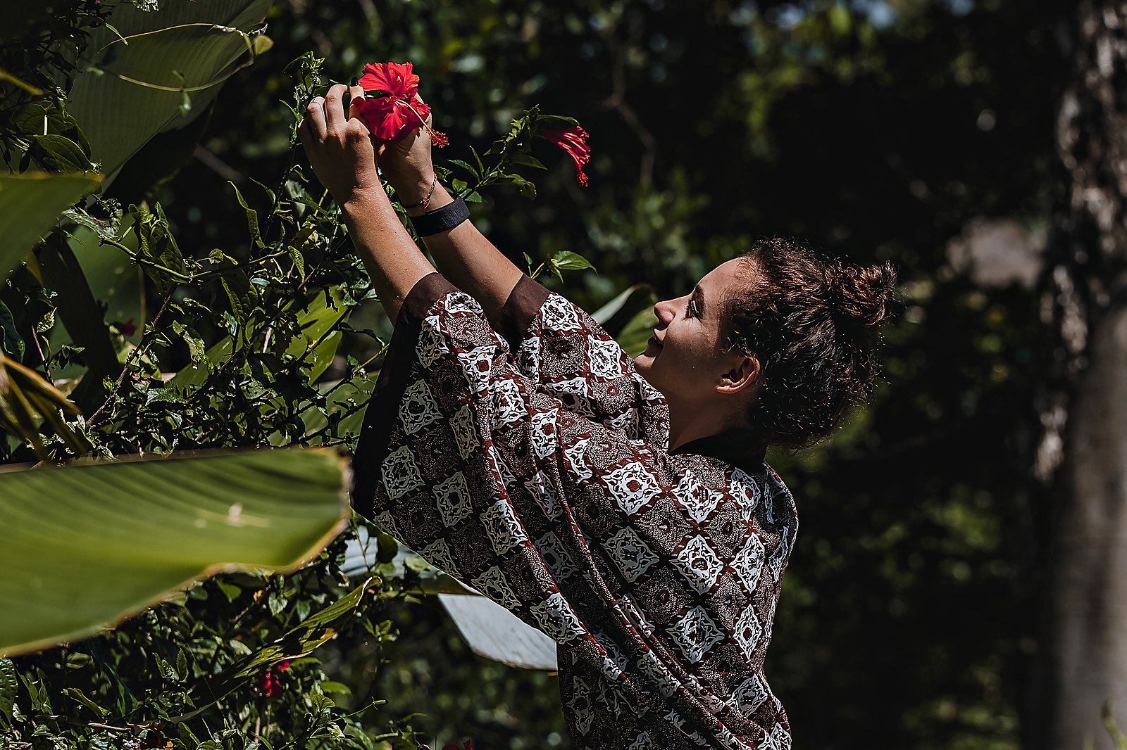 A guest in the hotel&rsquo;s batik robe reaching up to a red hibiscus in the garden