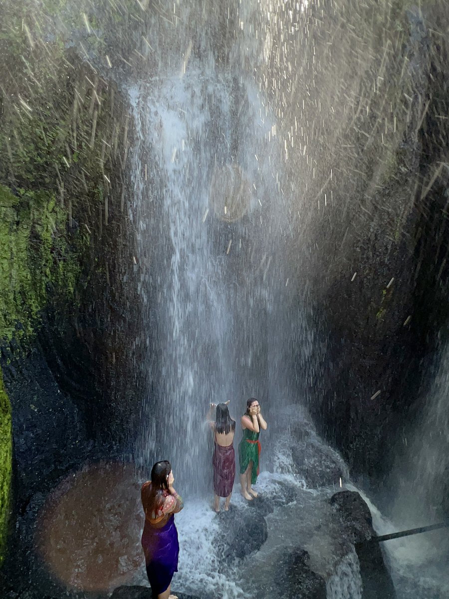 Three women standing under the falling water at the melukat springs