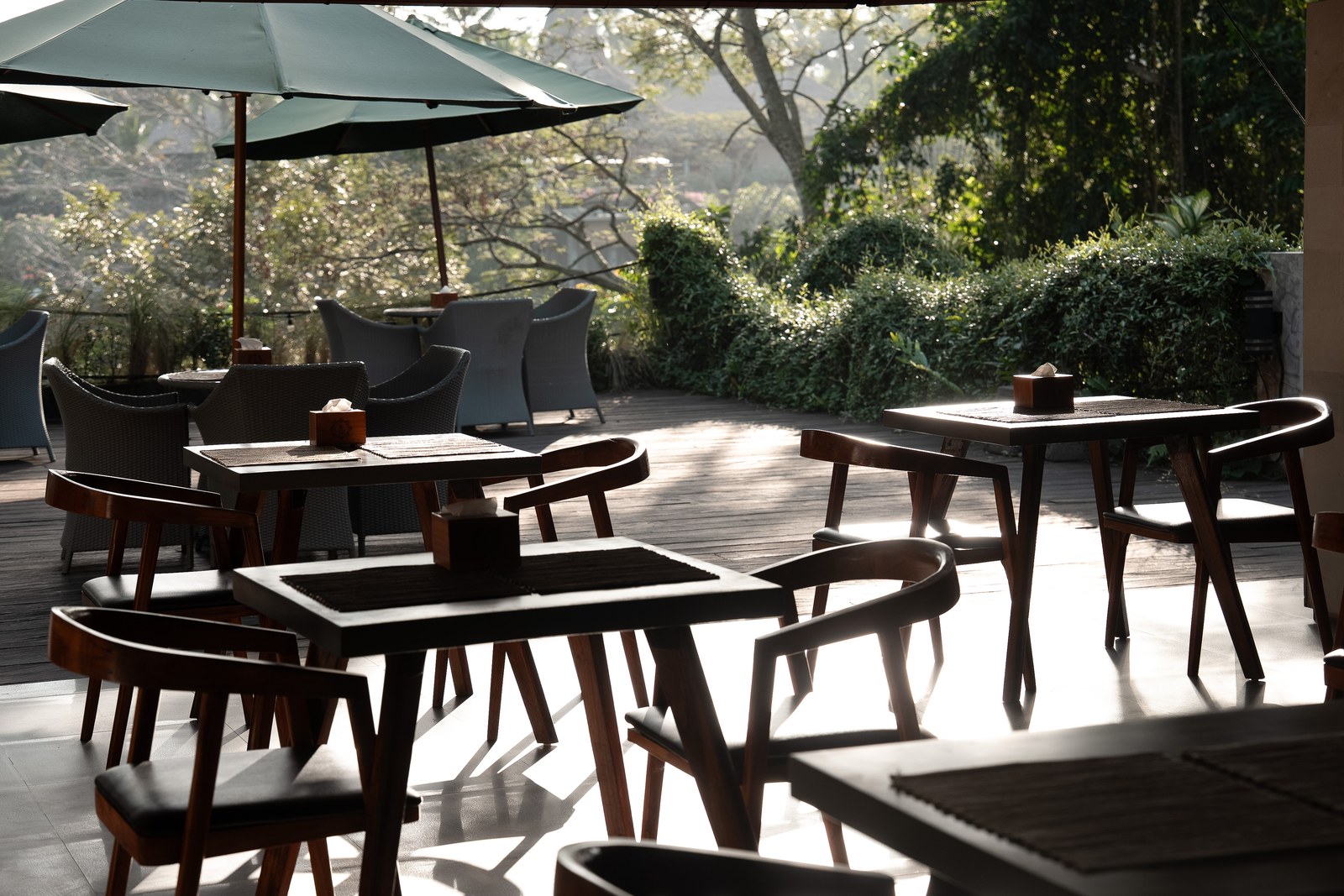 Tables on the restaurant terrace in low morning light, the garden behind