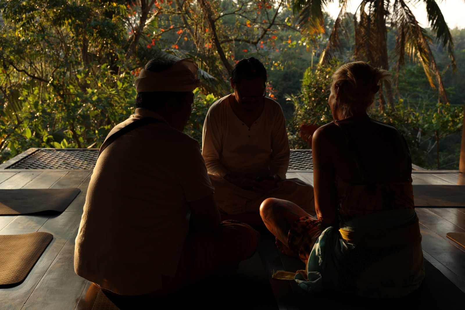 Three people talking in the shala at sunset, the jungle lit behind them