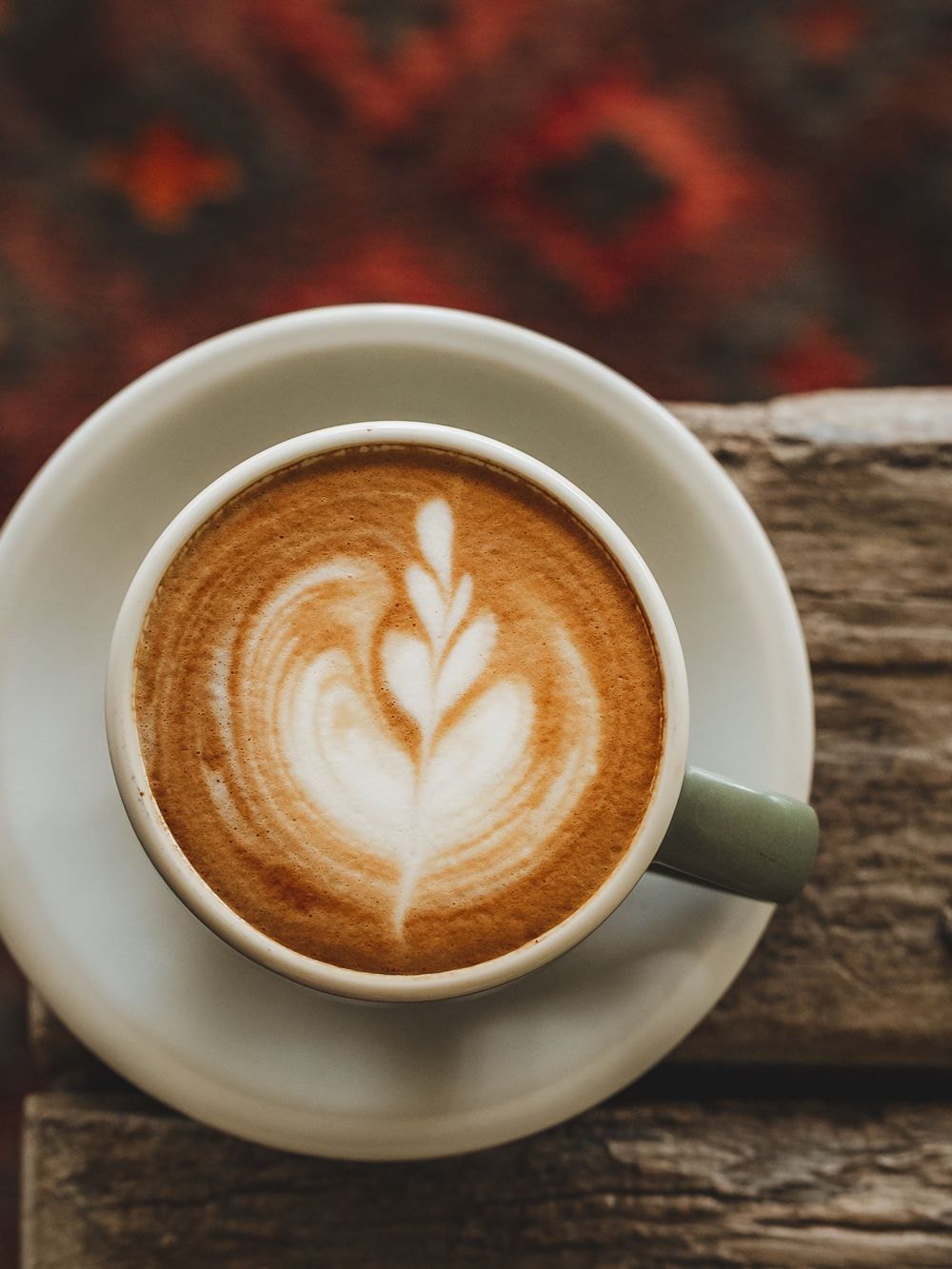 A latte on the edge of a wooden table, the kilim rug below