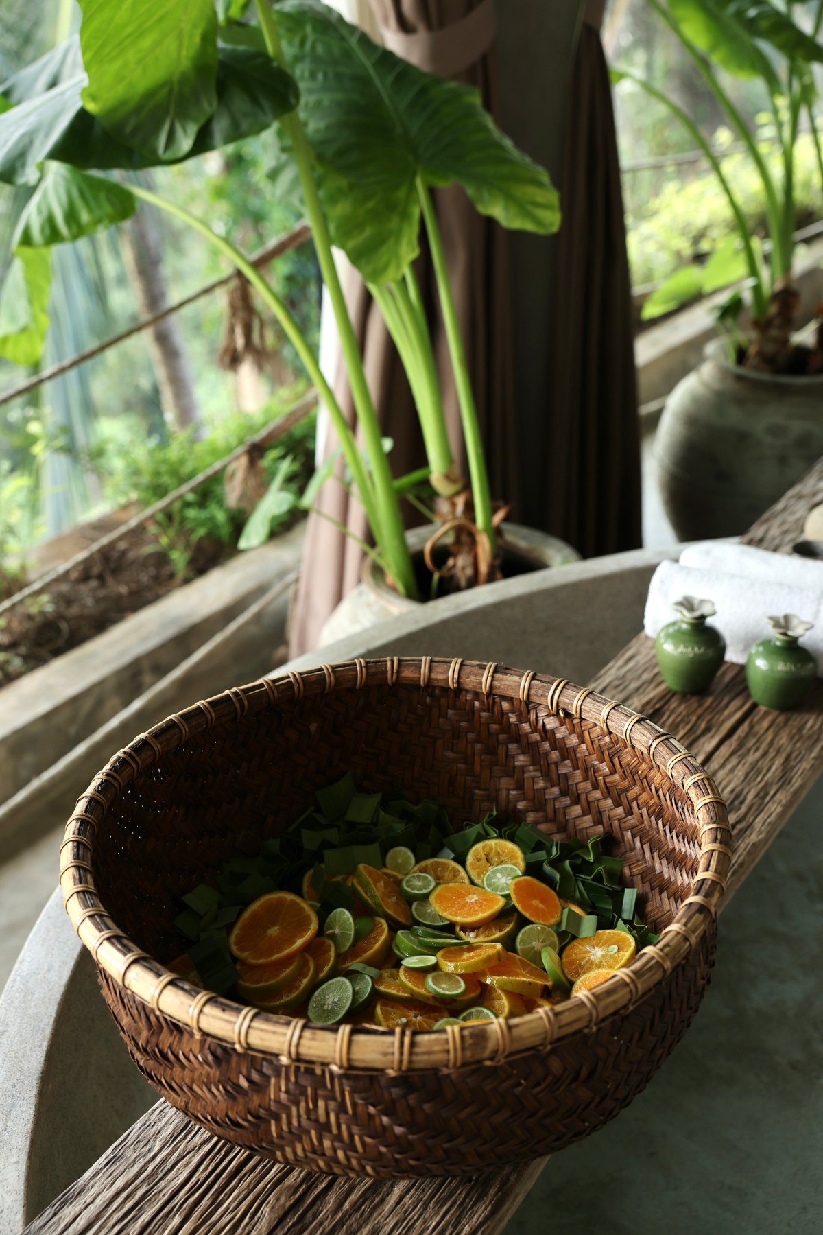 A rattan basket of sliced oranges, limes and green leaves on the edge of the bath