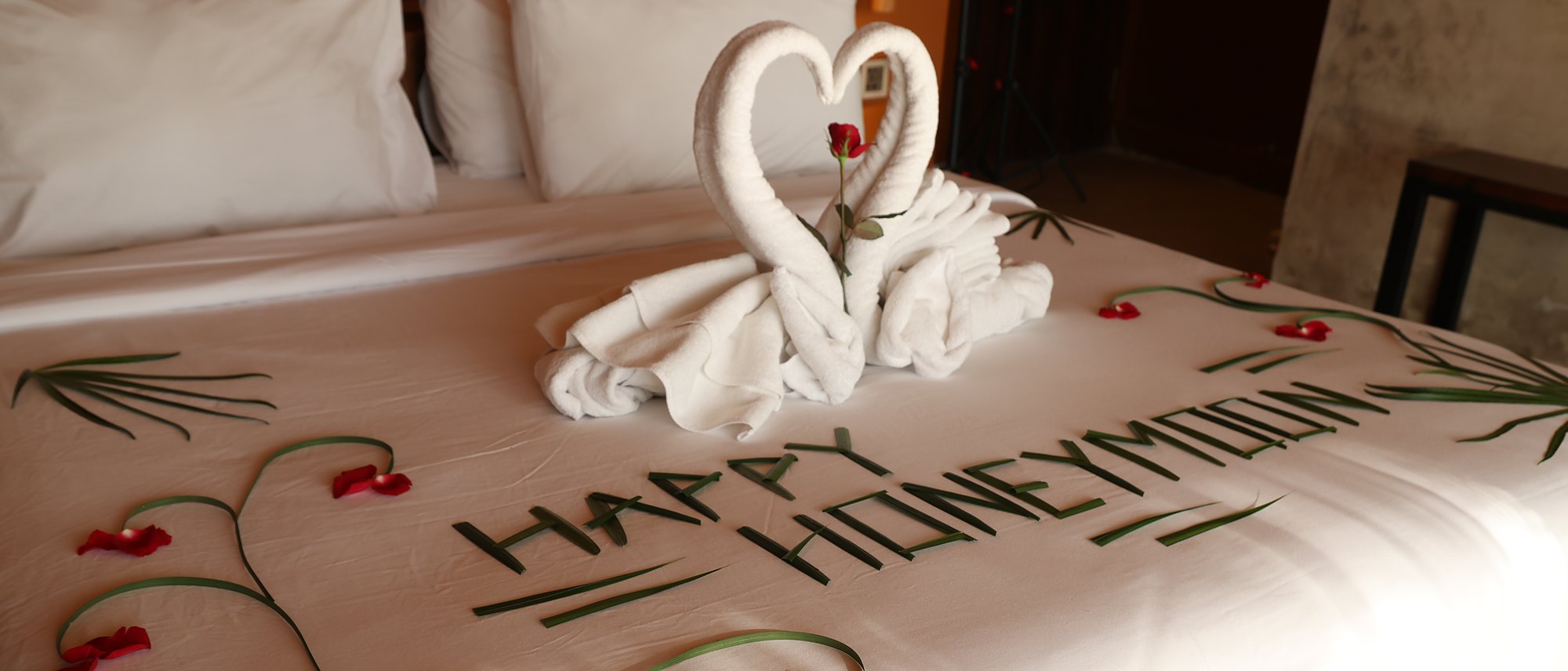 Towel swans, rose petals and a Happy Honeymoon greeting laid on the bed